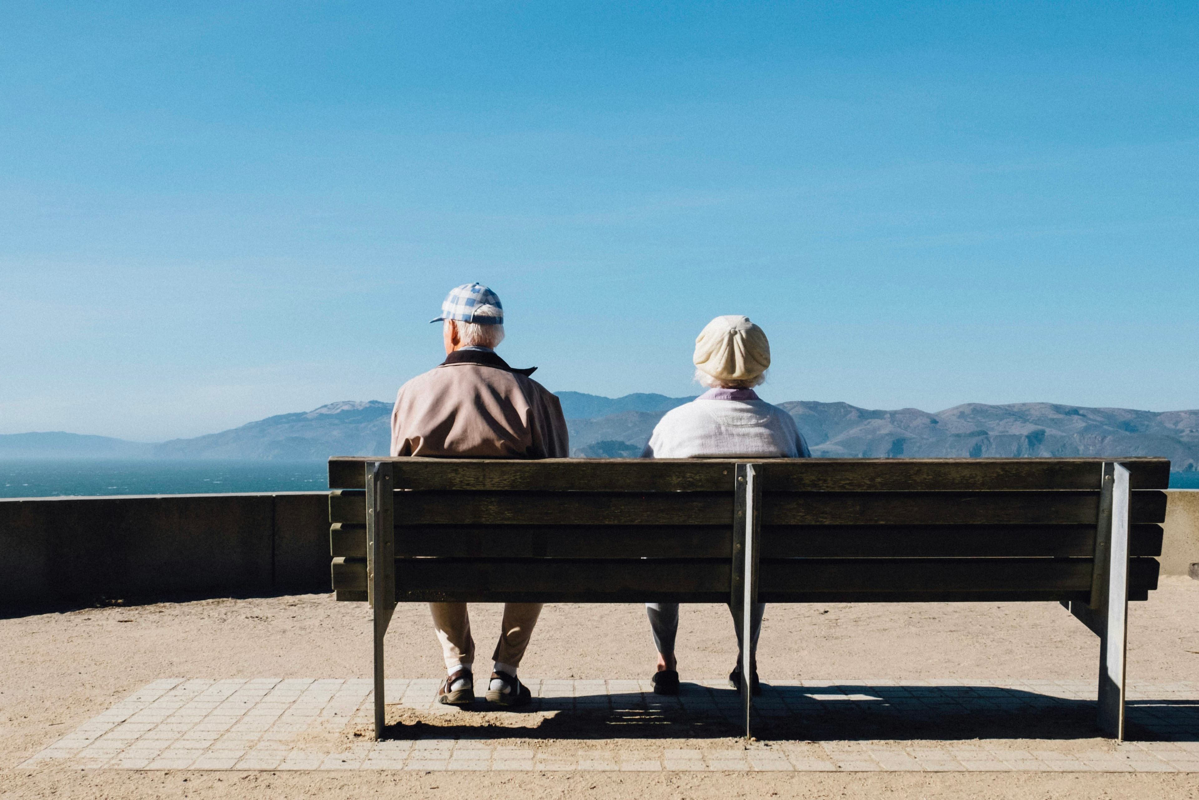 A man and woman sitting on a bench facing the sea