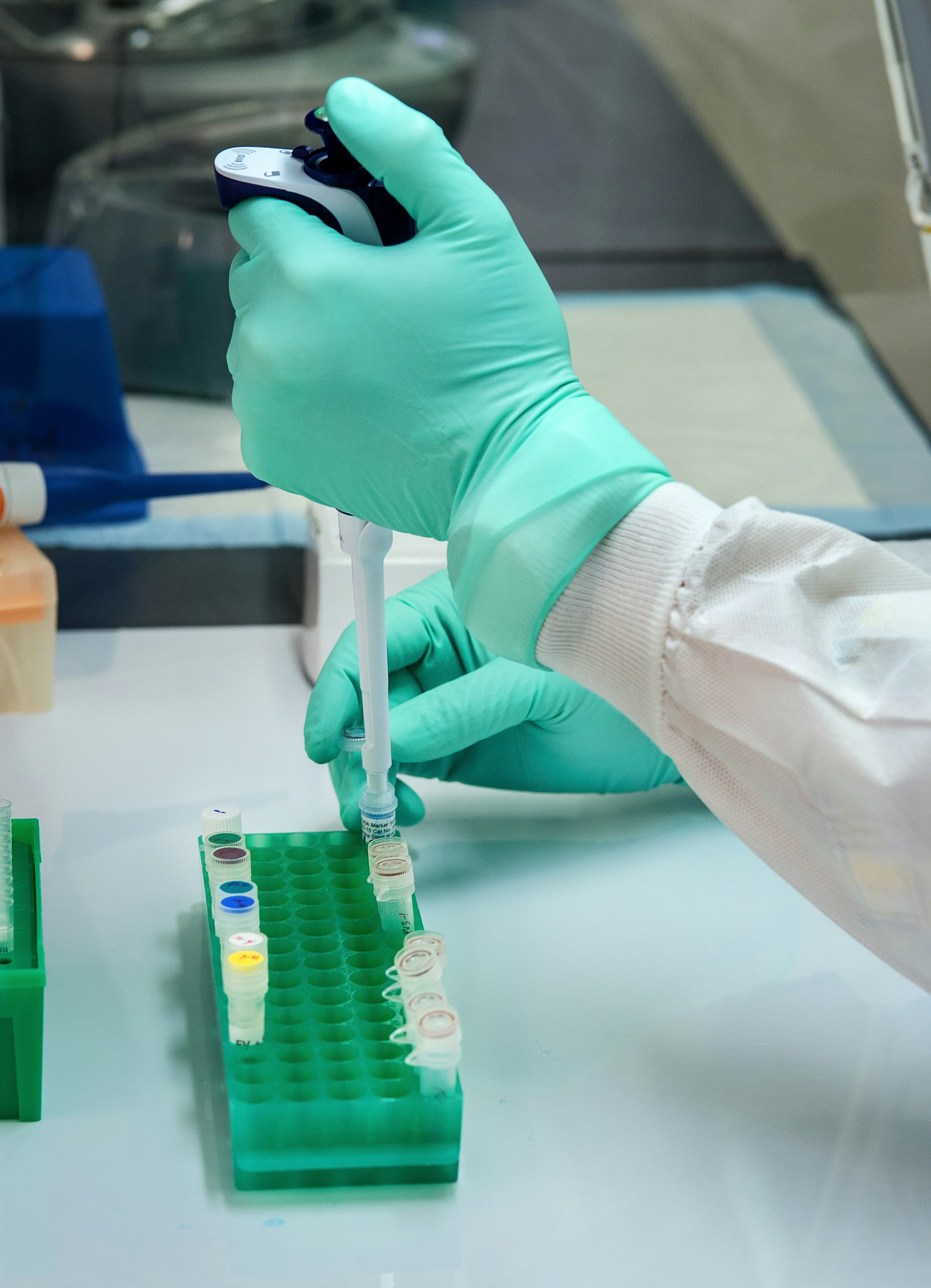 A person in green gloves using a pipette to fill a small vial