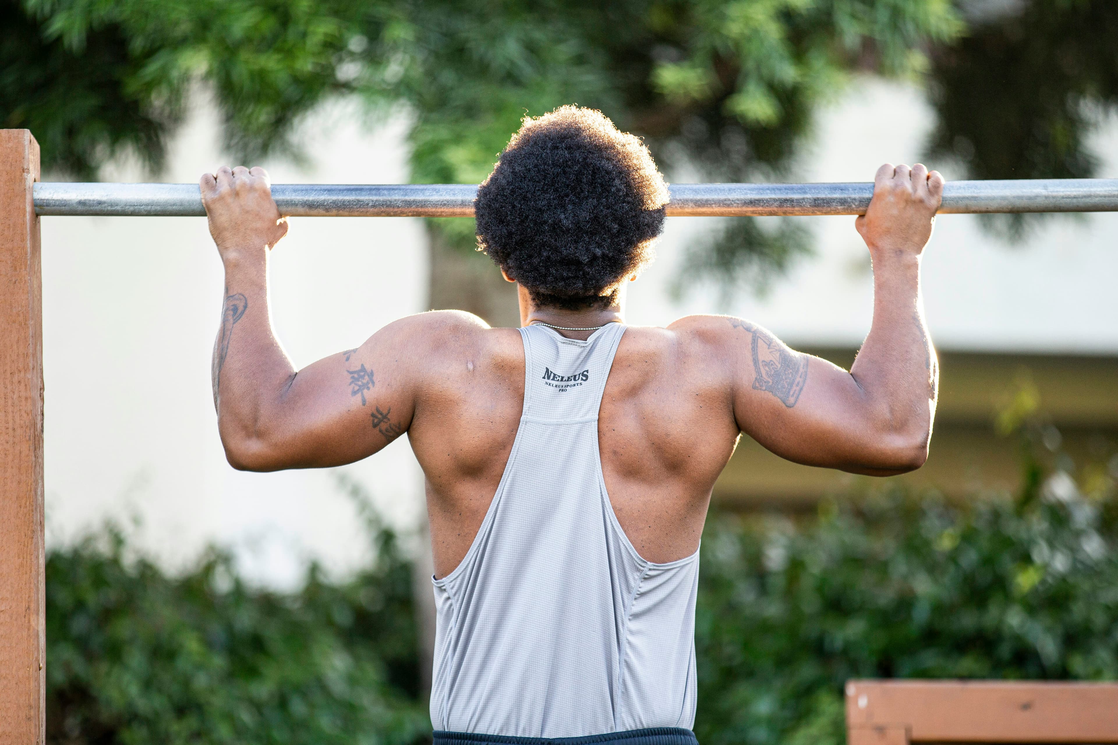 A man in a gray tank top gripping a metal pull-up bar