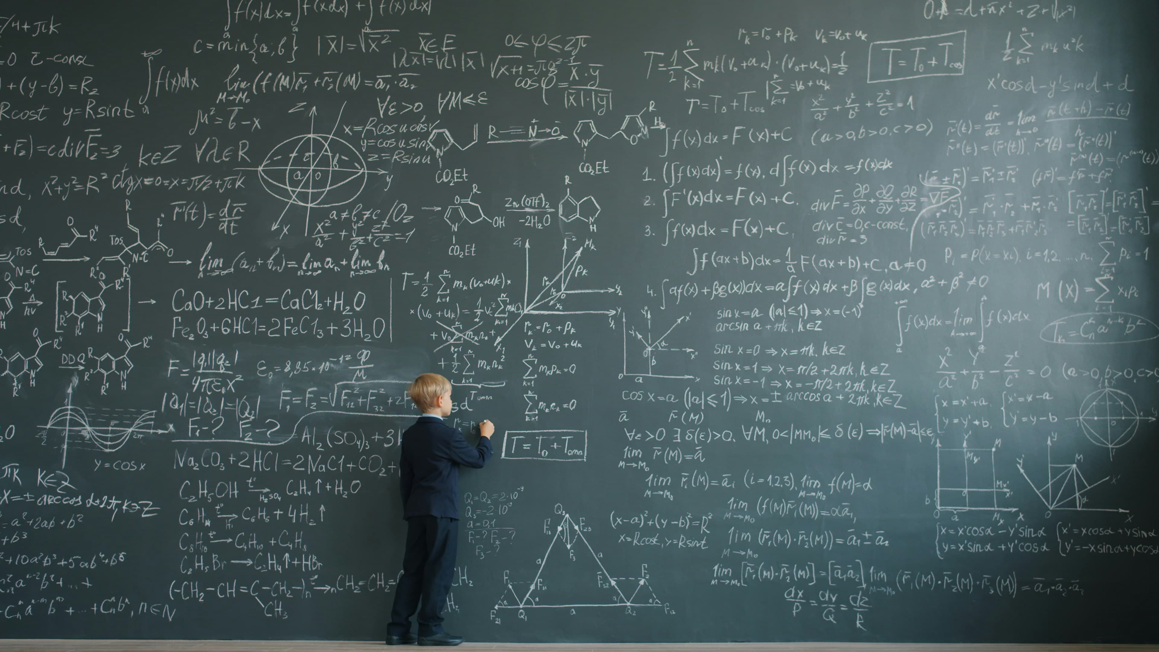 A young boy writing complex formulas on a chalkboard