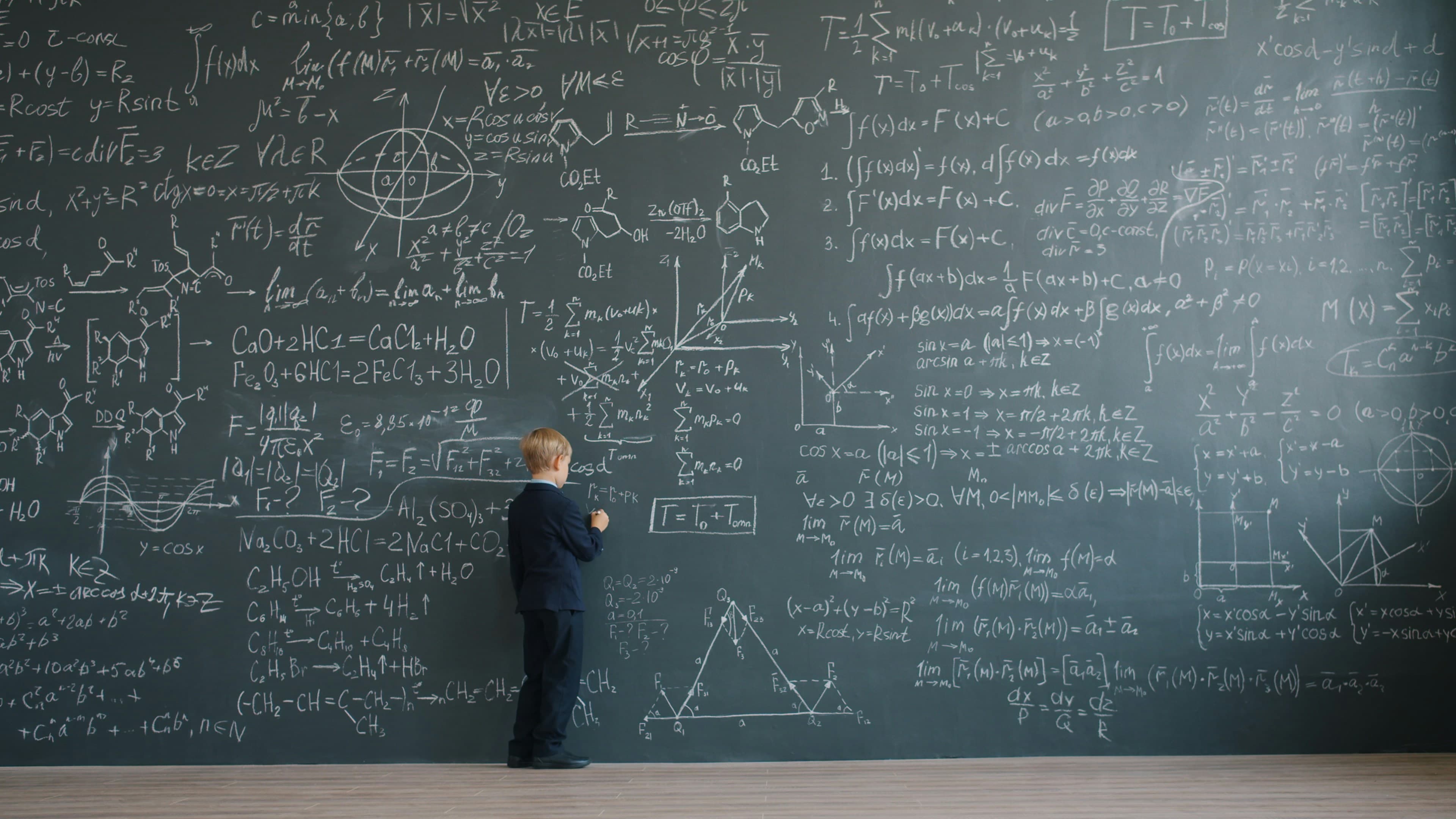A boy standing in front of a blackboard covered in equations