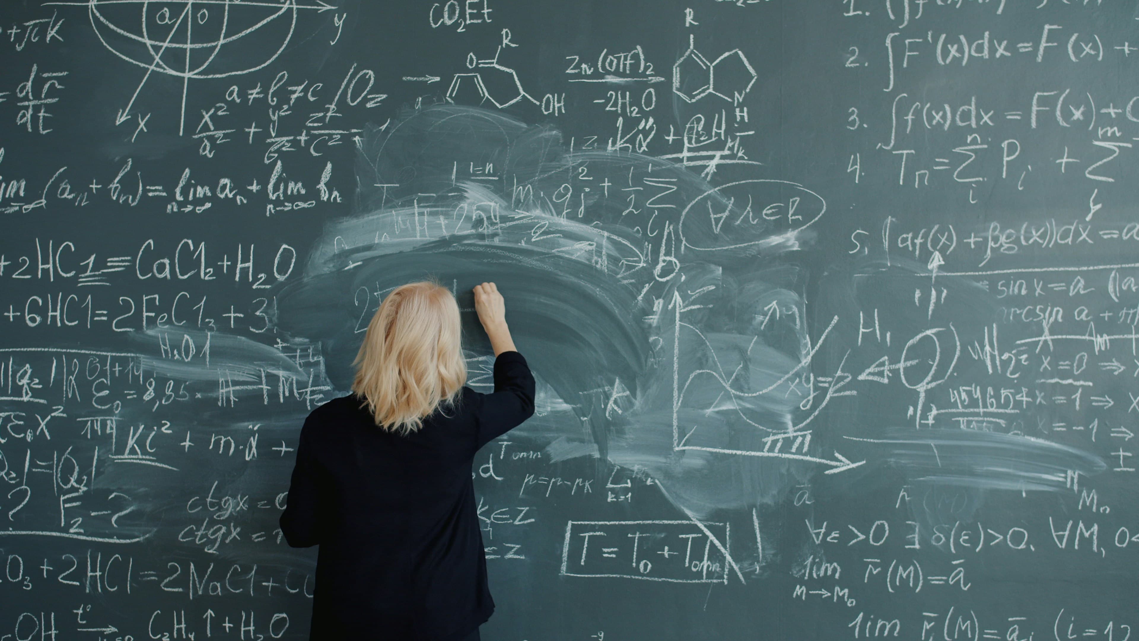 A woman writing mathematical formulas on a chalkboard