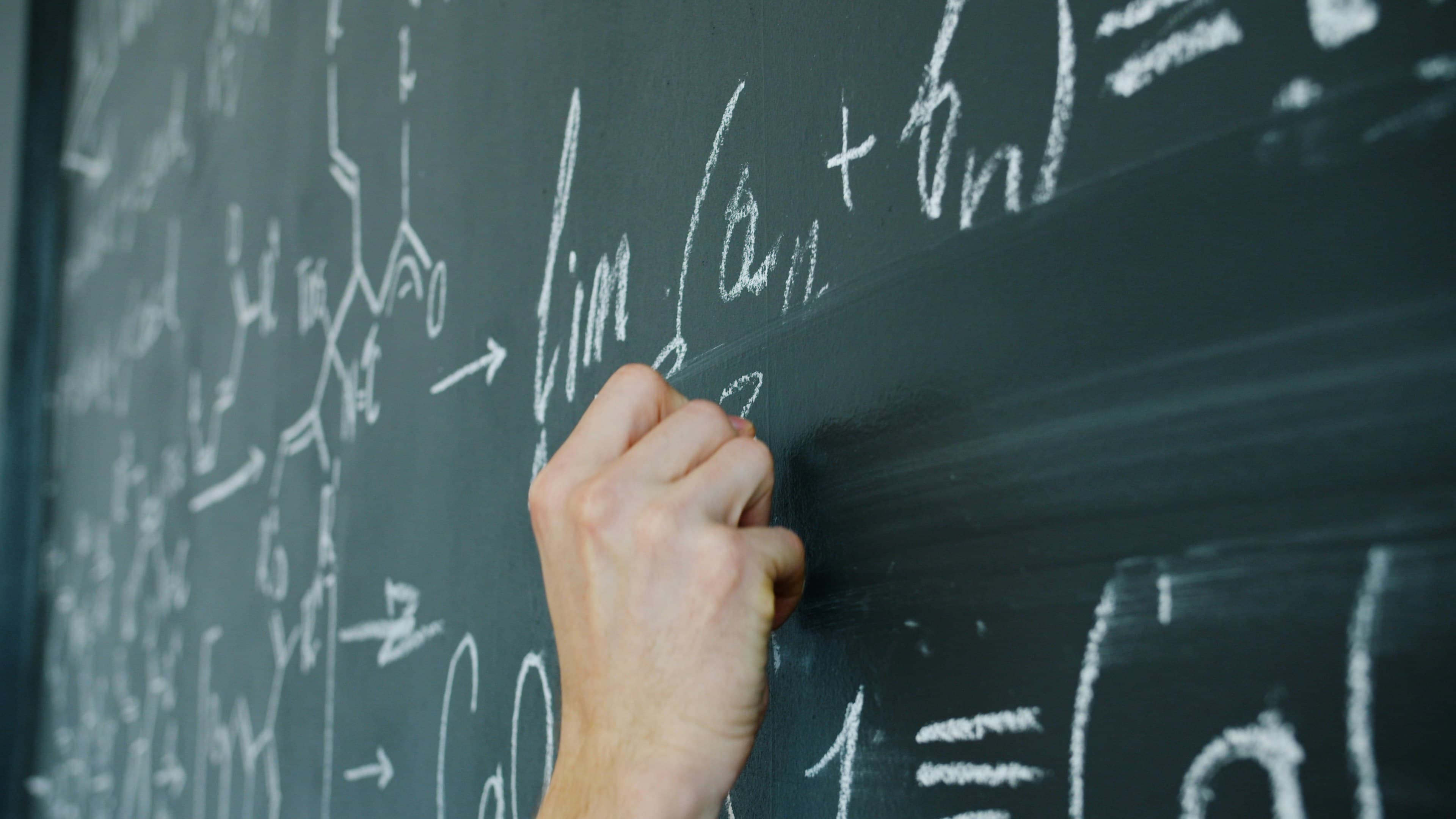 A hand writing mathematical formulas on a blackboard with chalk