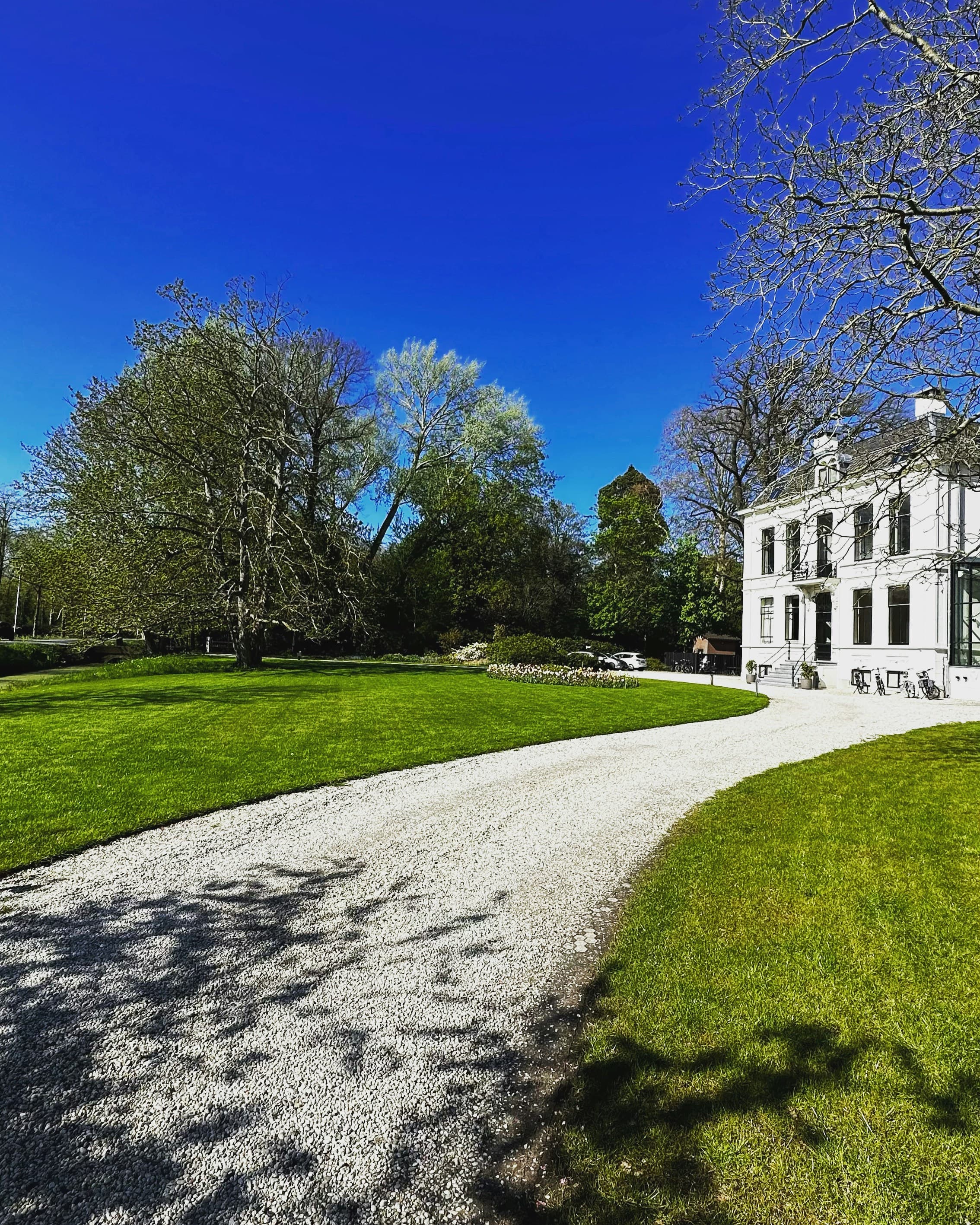 White manor house with a gravel driveway and green lawn
