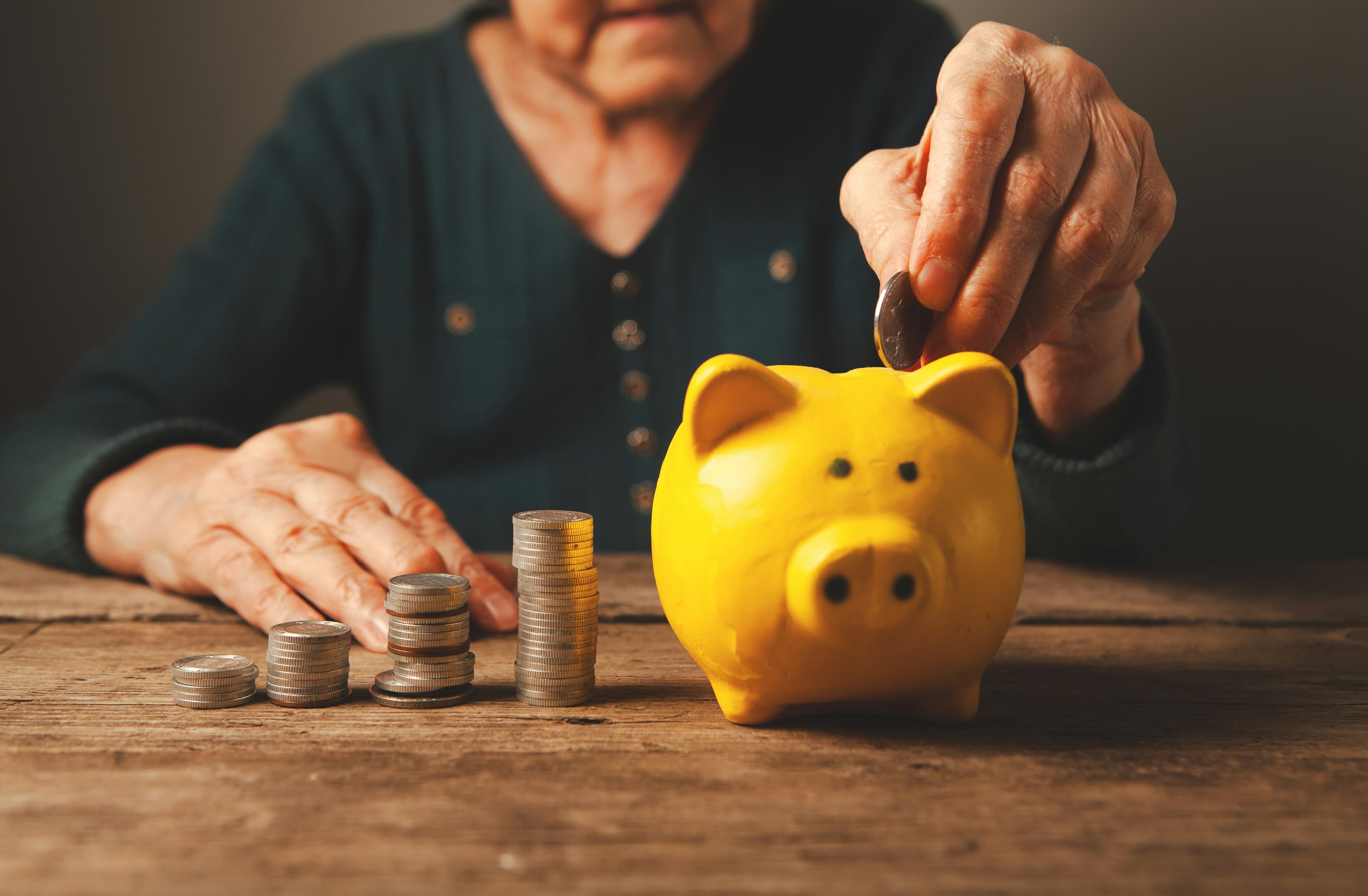 Elderly hands dropping coins into a yellow piggy bank