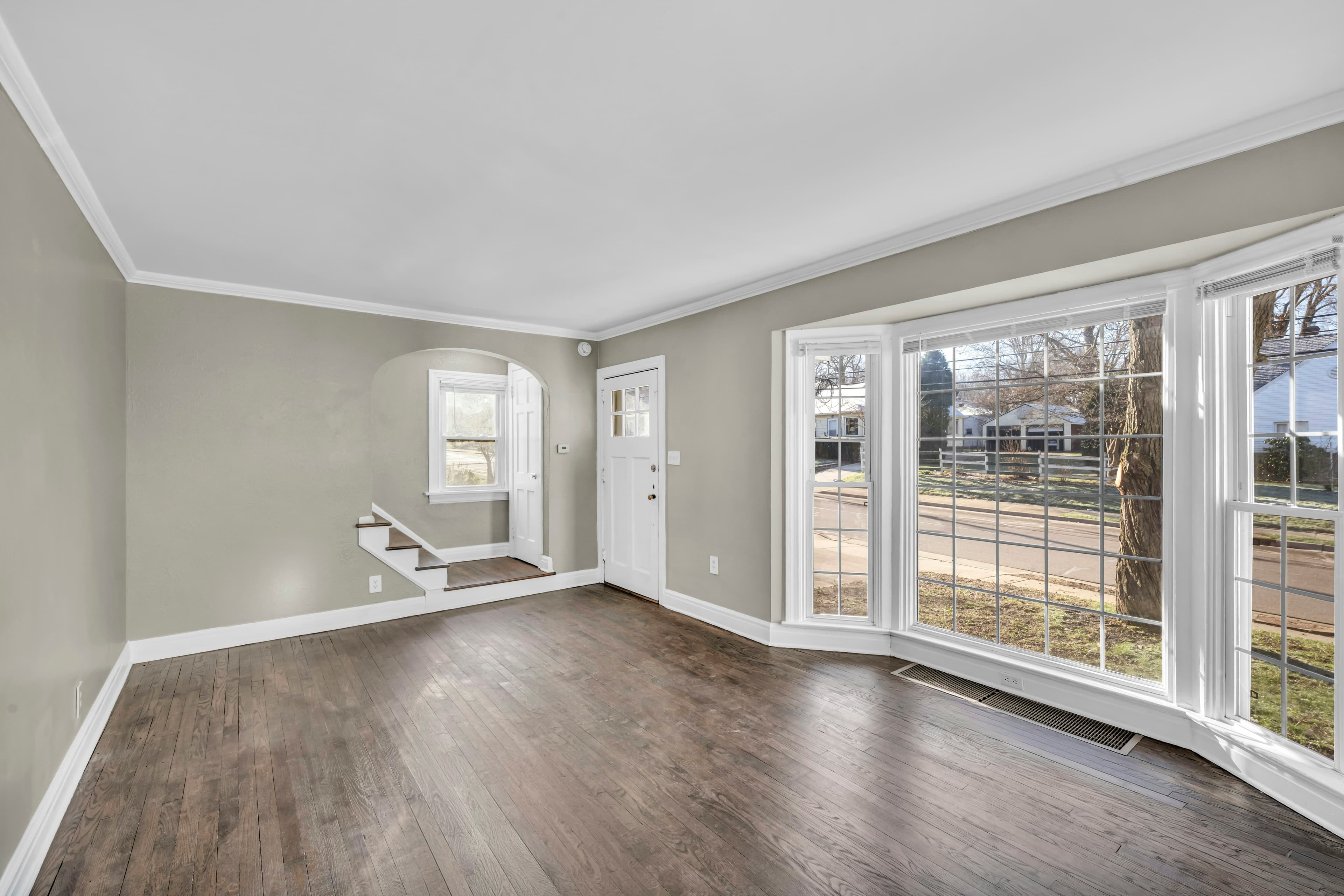 A spacious empty living room with a bay window and gray walls
