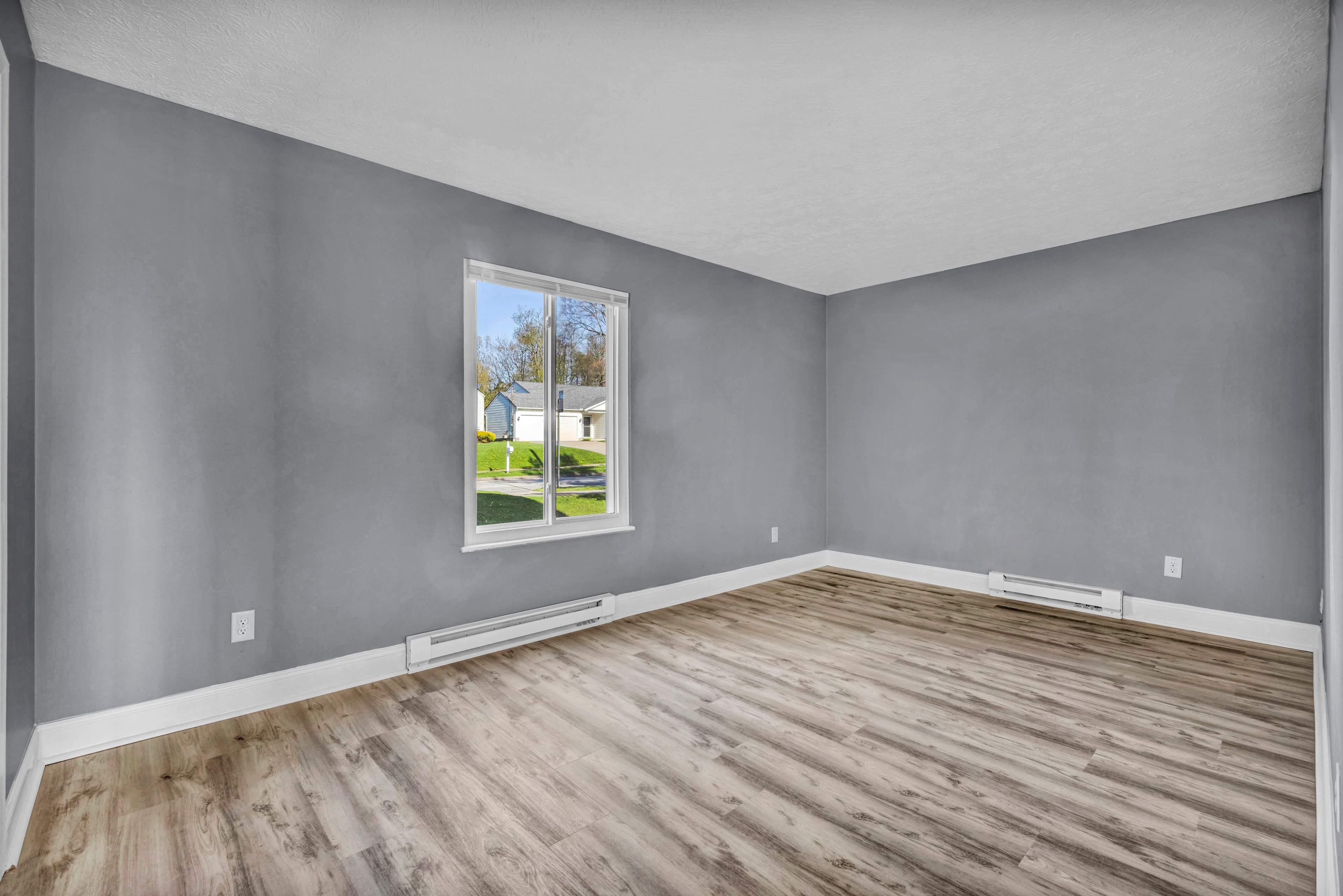 An empty room with gray walls, white trim and light wood-look flooring